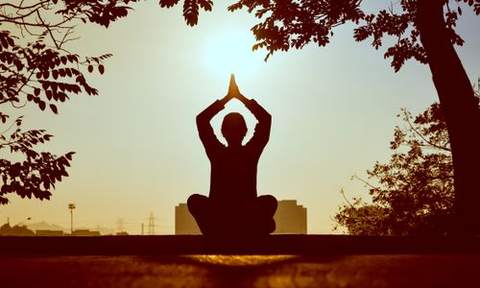 A person sitting cross-legged in silhouette at sunrise